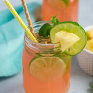 A cherry pineapple mojito in a glass mason jar with two straws and lime slice garnish.