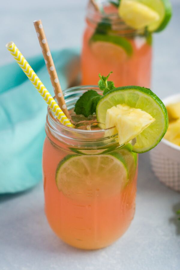 A cherry pineapple mojito in a glass mason jar with two straws and lime slice garnish.