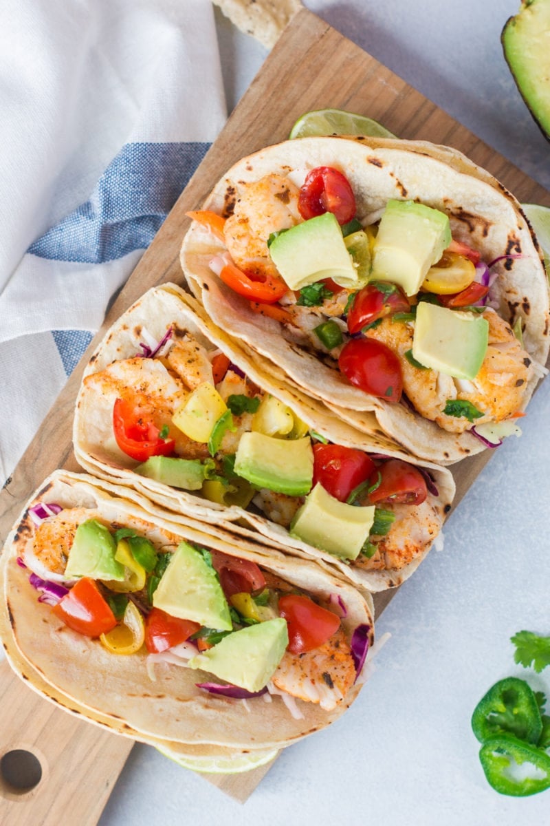 Three fish tacos topped with slaw, tomatoes and avocado.