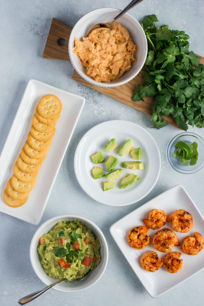 Overhead shot of plates with crackers, shrimp, guacamole and avocado.