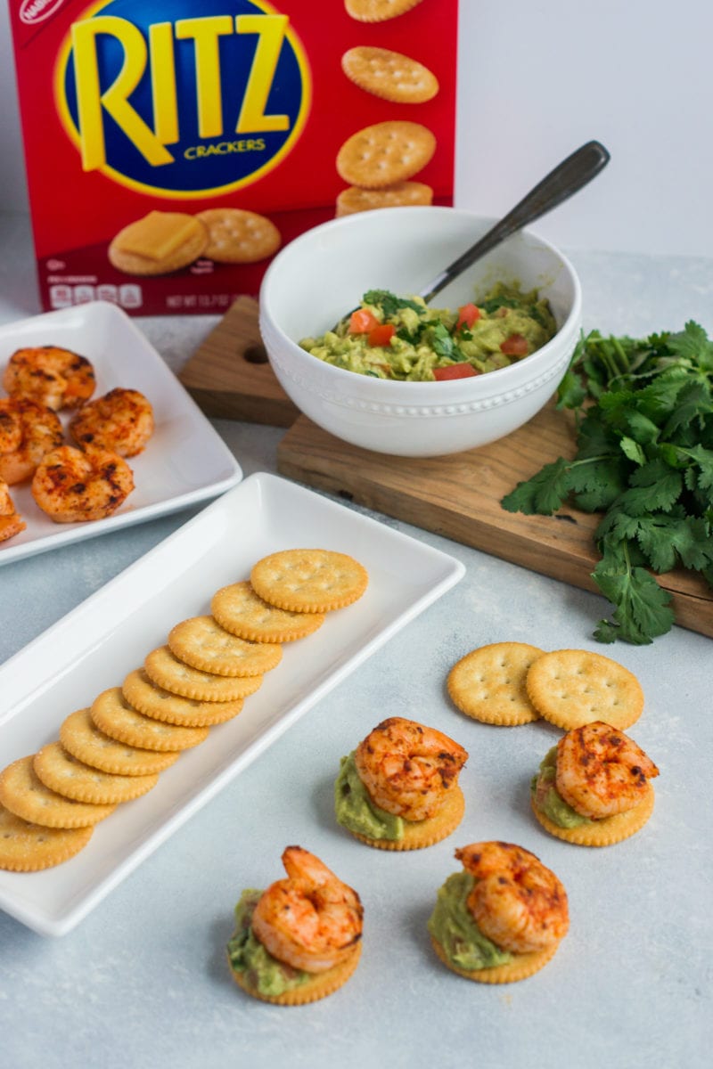 Crackers, shrimp and guacamole on plates next to the made up appetizers.