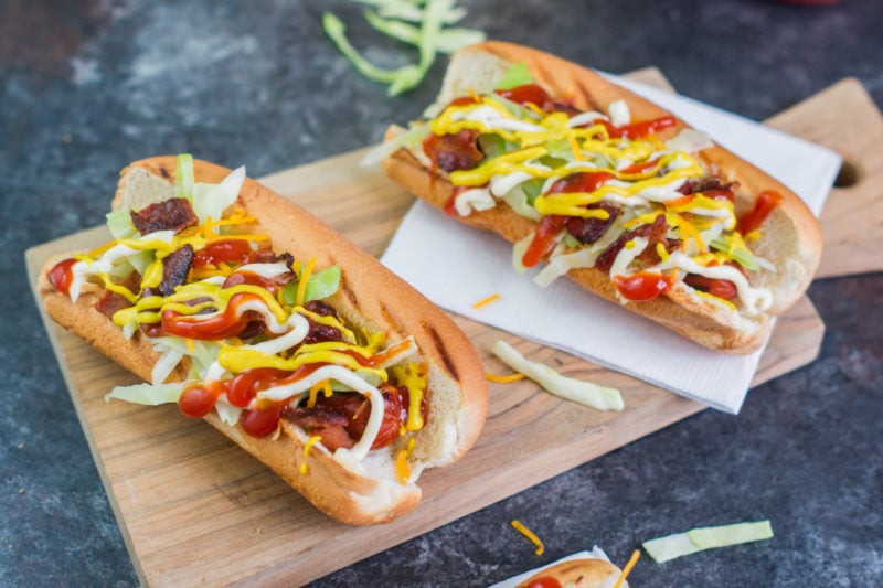 Two Dominican style hot dogs on a wooden serving board.