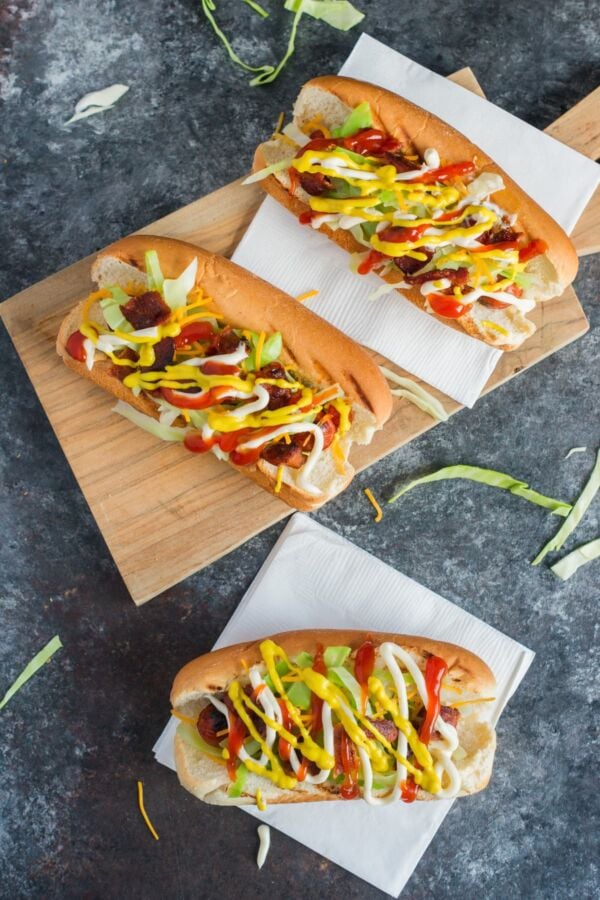 Three Dominican style hot dogs on a wooden chopping board.