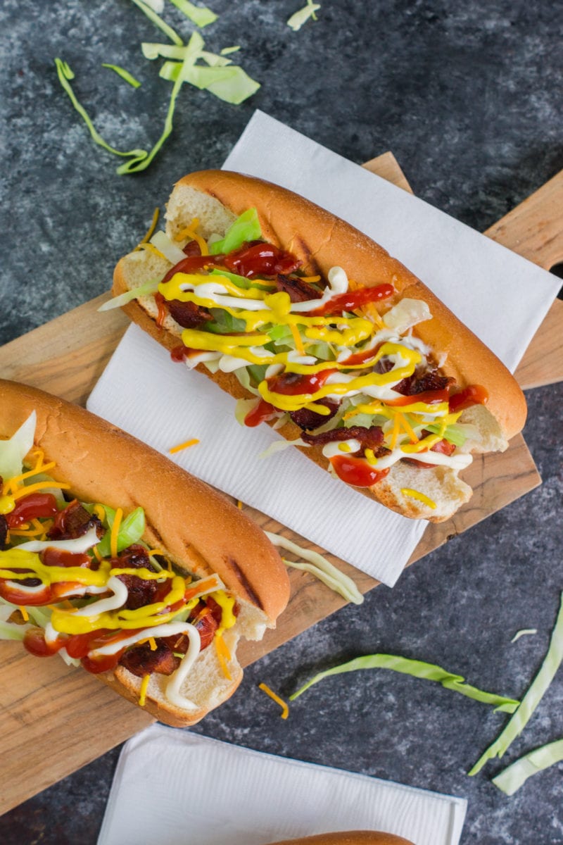 Two hot dogs on a wooden serving board.