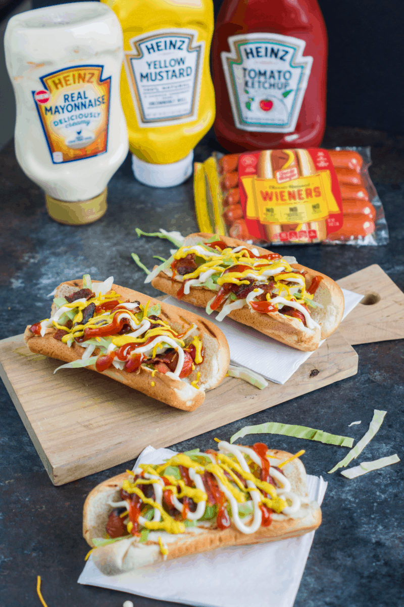 Three hot dogs next to bottles of condiments.