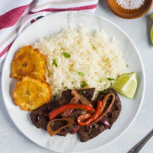 Overhead shot of liver and onions srevd with rice, tostones and a wedge of lime.