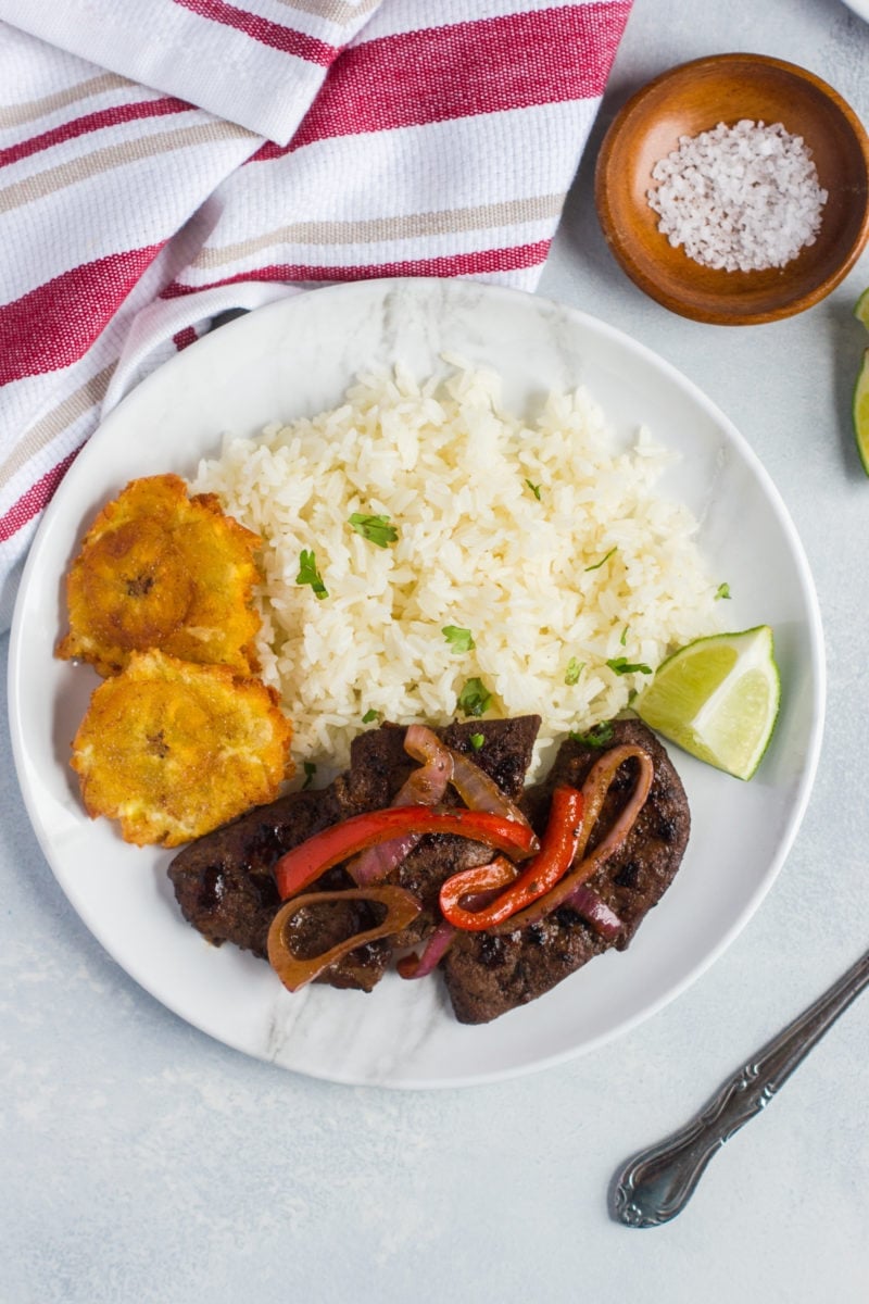Overhead shot of liver and onions srevd with rice, tostones and a wedge of lime.
