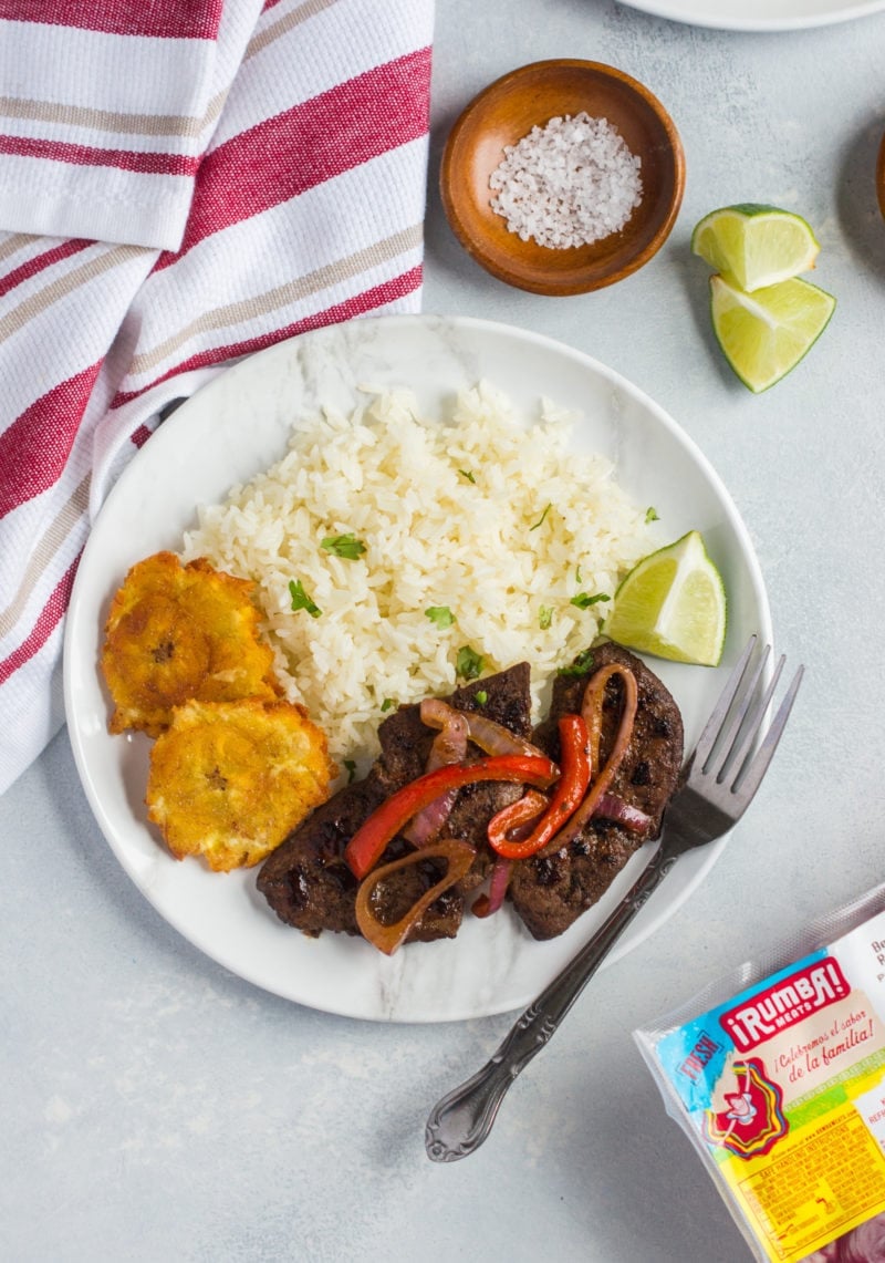 Liver and onions served on a plate with rice and lime wedges.