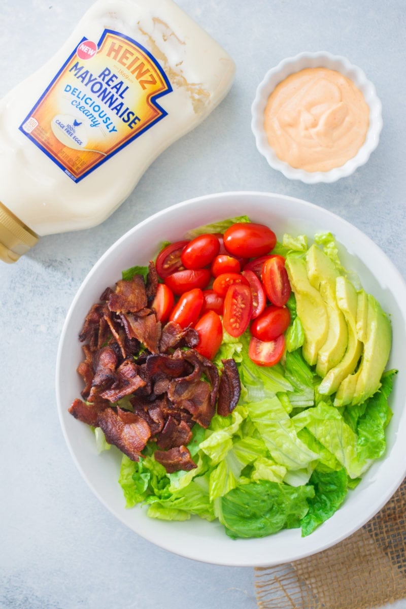 A BLT salad in a large white bowl before being tossed and dressed.