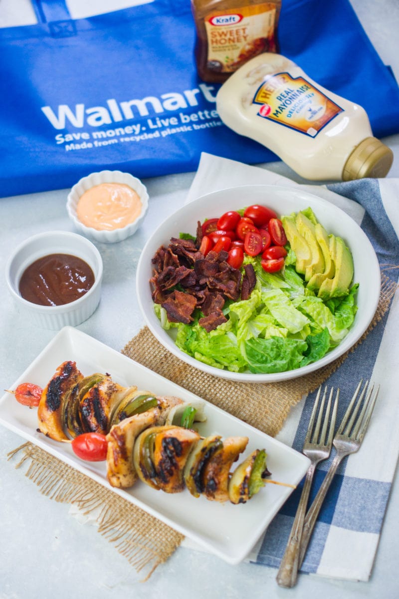 Chicken skewers and a salad bowl next to two sauces.