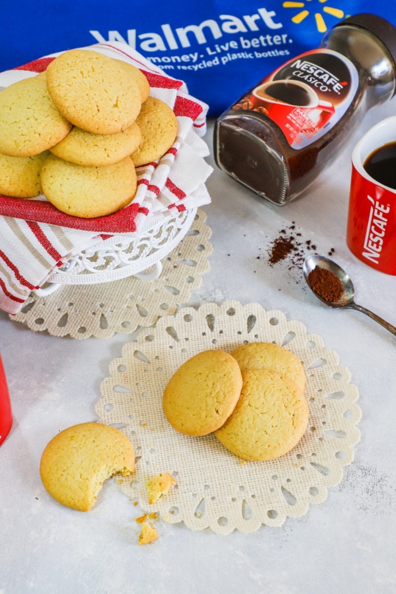 Butter cookies on a paper mat next to a spoon of coffee.