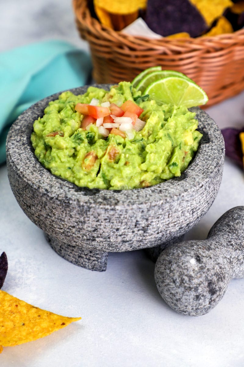 Guacamole piled high in a heavy stone bowl with garnishes.