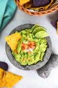 Guacamole served in a bowl with a tortilla chip and fresh lime slices.