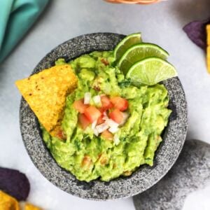 Guacamole served in a bowl with a tortilla chip and fresh lime slices.