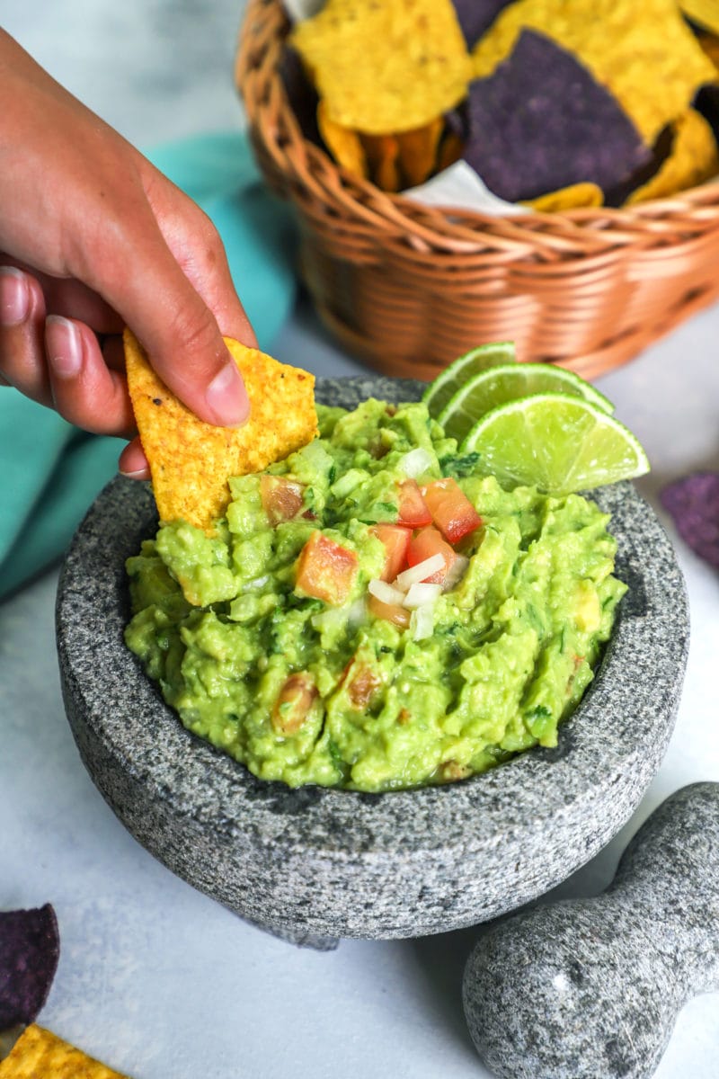 A hand holding a tortilla chip, dipping into the guacamole.