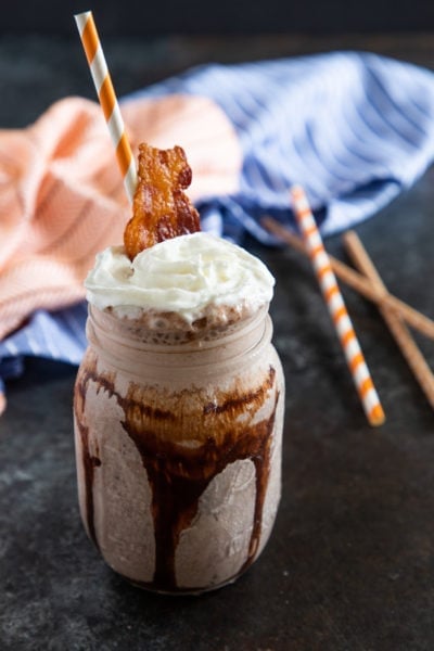 A bourbon milkshake in a mason jar topped with whipped cream and a piece of crispy bacon.