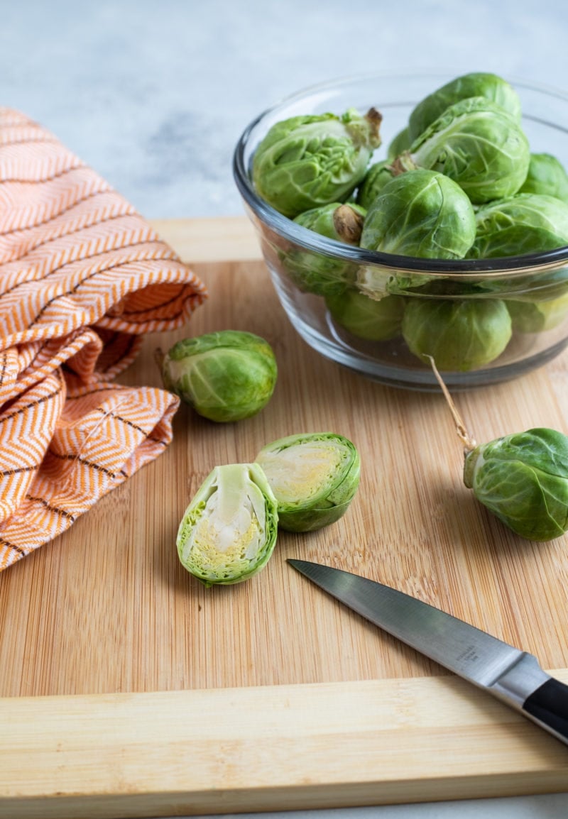 Brussels sprouts being cut in half on a wooden chopping board.