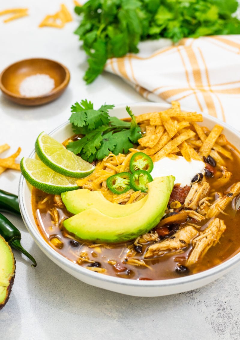 Sopa de tortilla con pollo servida en un bowl con queso, limon y aguacate. 