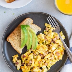 Ham and cheese egg scramble on a plate with toast and sliced avocado.