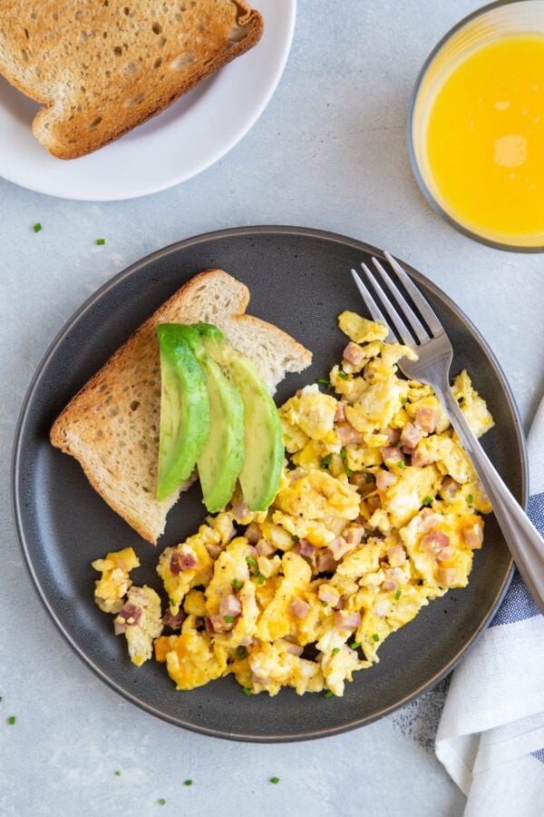 Ham and cheese egg scramble on a plate with toast and sliced avocado.