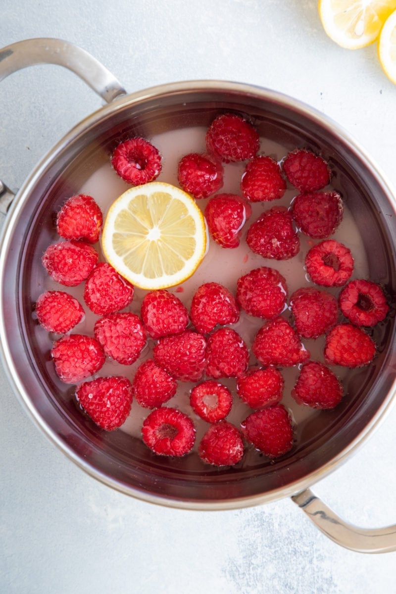 Fresh raspberries, lemon and sugar water in a pot.