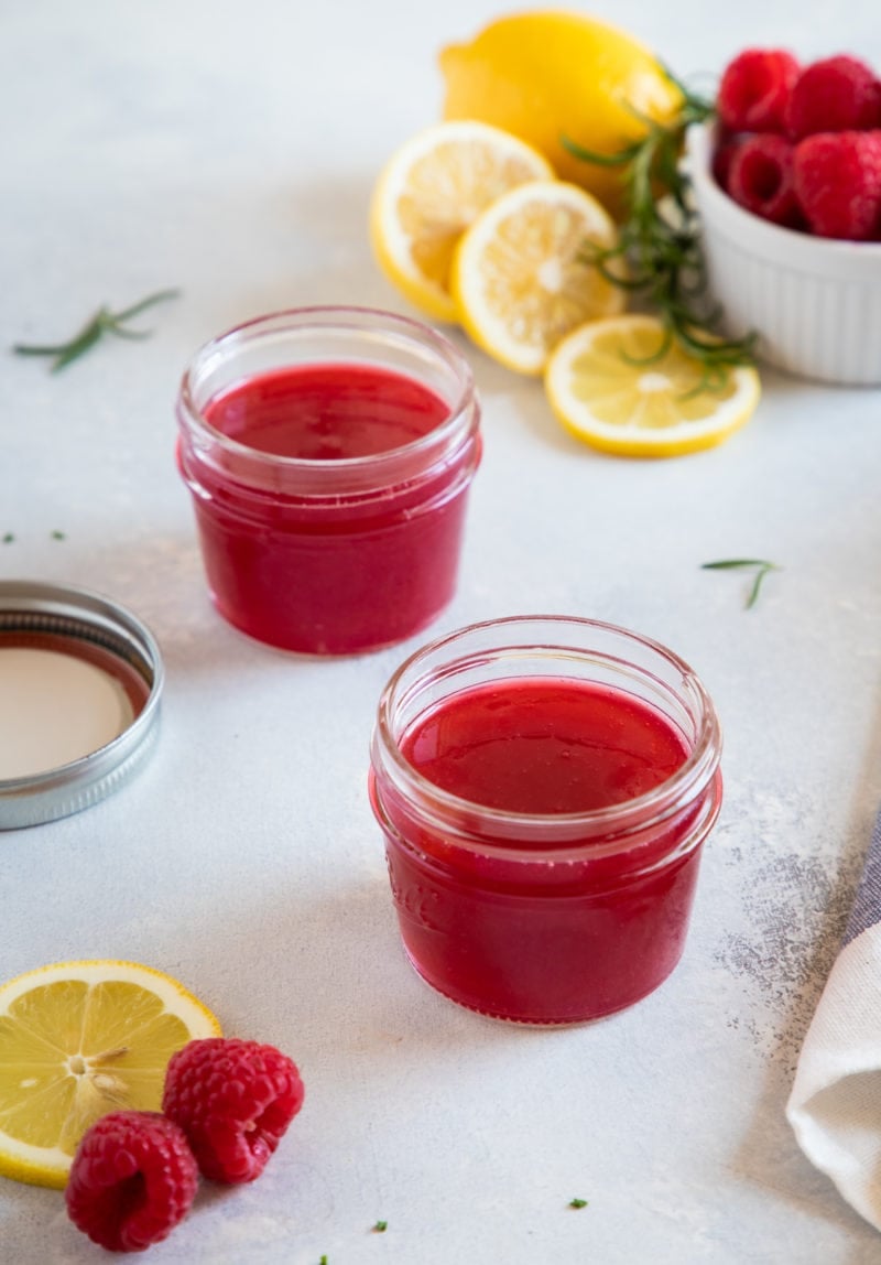 Two jars of the raspberry simple syrup next to slices of fresh lemon.