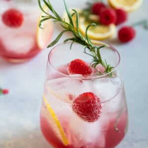 raspberry lemon wine spritzer served in a glass with lemon slices, raspberries and rosemary for garnish