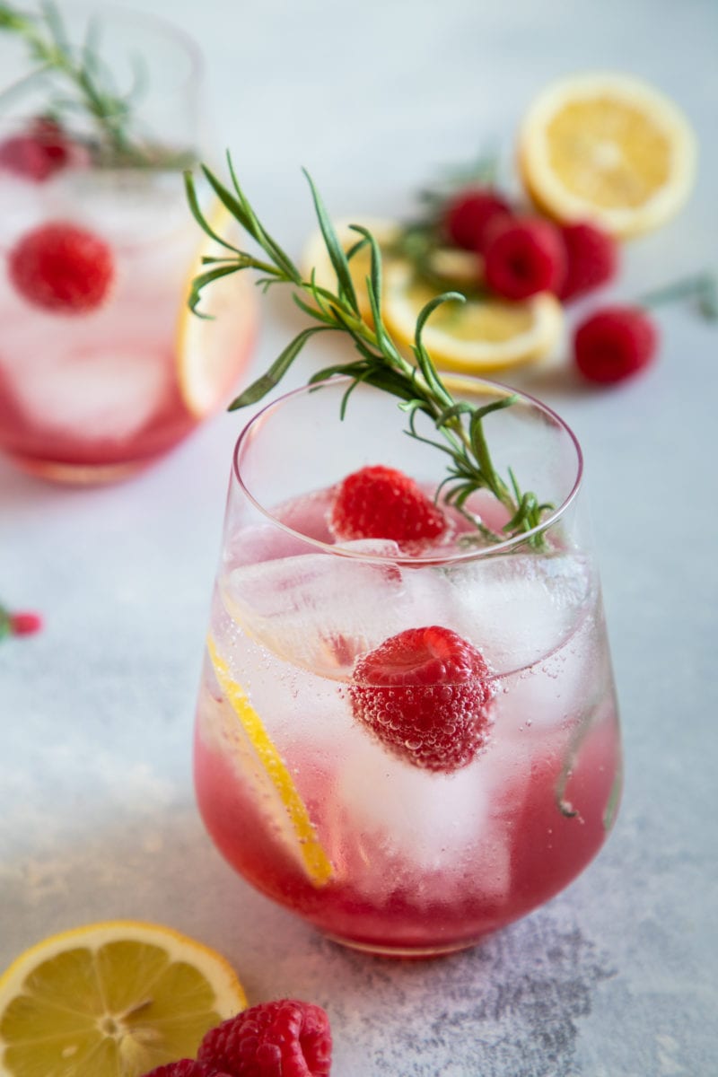 Spritzer de vino con limón y frambuesa servido en un vaso con rodajas de limón, frambuesas y romero para decorar