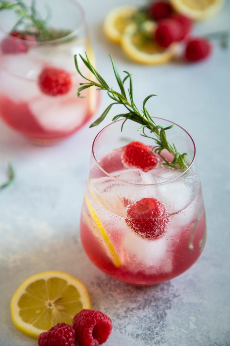 Spritzer de vino con limón y frambuesa servido en un vaso con rodajas de limón, frambuesas y romero para decorar