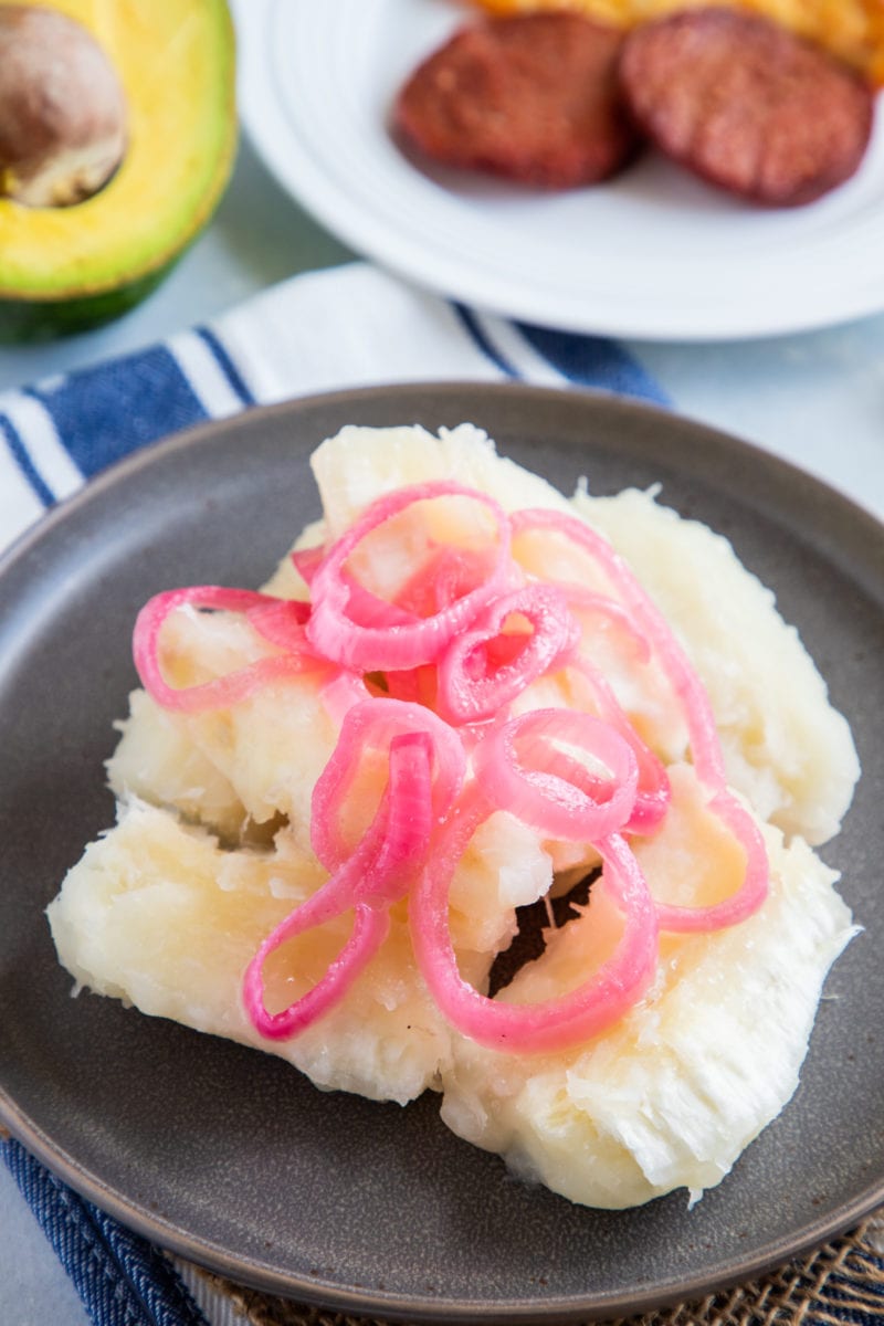 Boiled Yuca served on a plate and topped with onions.