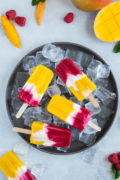 Overhead shot of four mango raspberry popsicles laid on top if ice cubes.