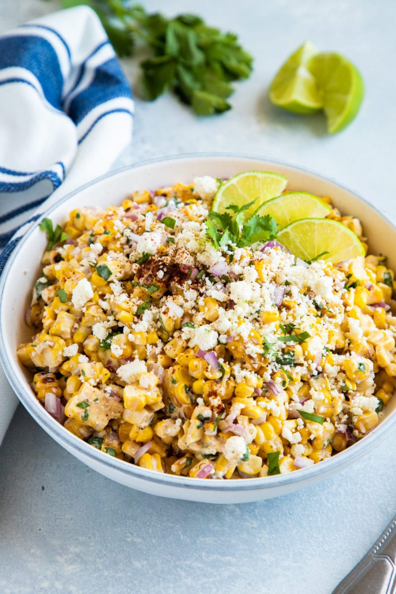 Ensalada Mexicana de Maiz a la parrilla servida en un plato hondo con queso cotija, cilantro y rebanadas de limón. 