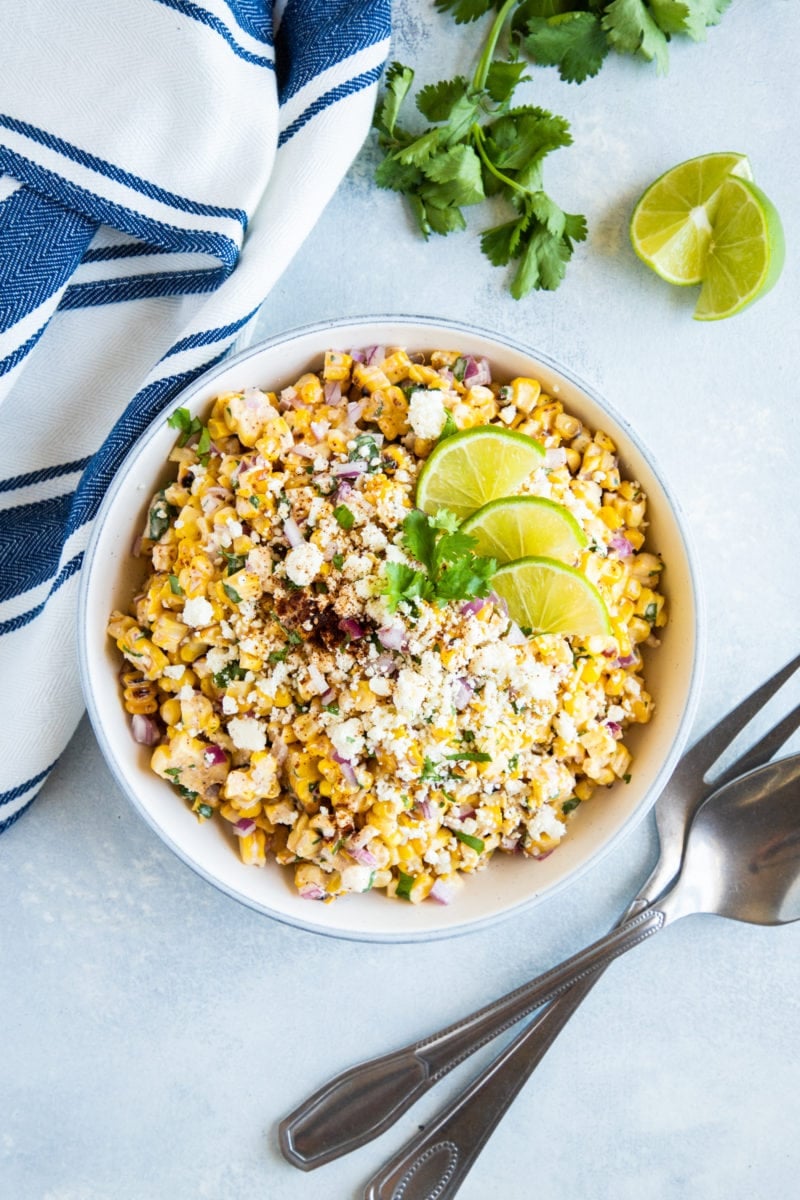 Mexican Grilled Corn salad served in a shallow bowl topped with cotija cheese, cilantro and lime slices. 
