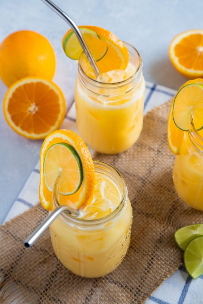 Juice served in mason jars garnished with orange slices and a metal straw. 