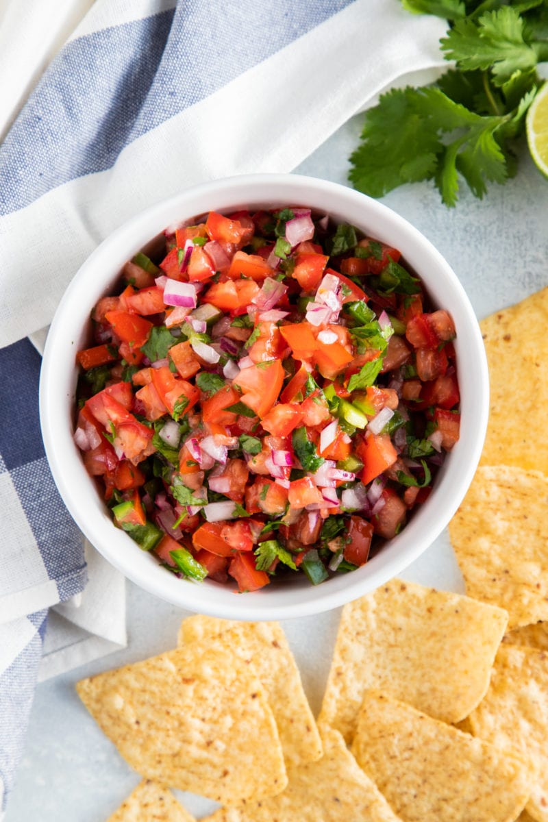 Pico de Gallo salsa in a white bowl with tortilla chips on the side. 