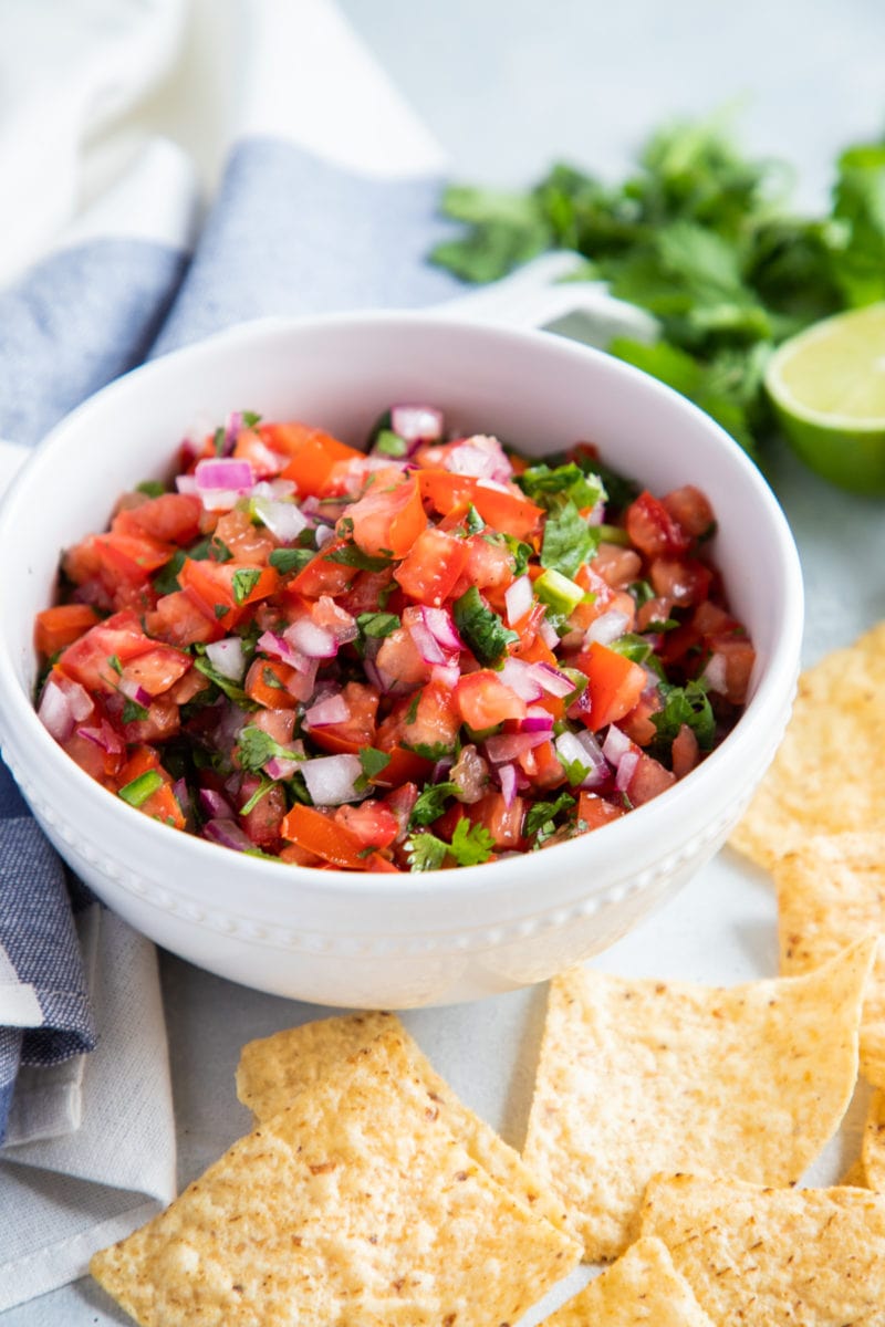 Pico de Gallo salsa in a white bowl with tortilla chips on the side. 
