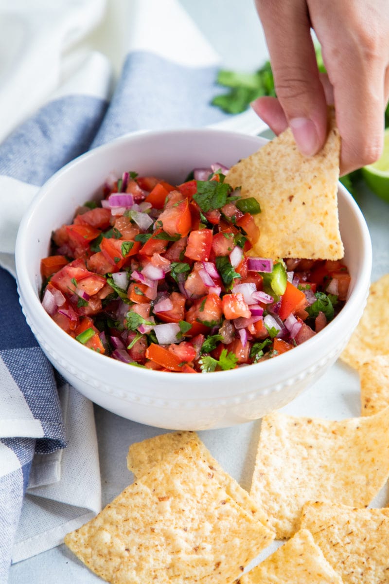 Hand dipping a tortilla chip in the bowl with pico de gallo. 
