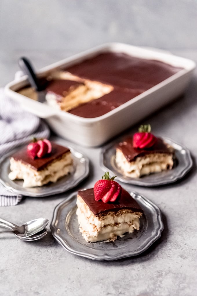 Slices of eclair cake served on three plates with fresh strawberries.