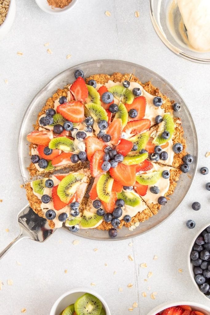 A fruit pizza on a plate cut into slices.