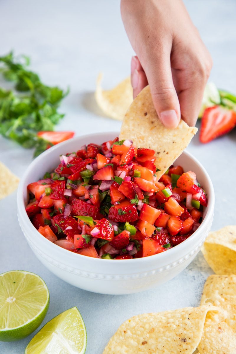 Hand dipping a corn chip into a bowl filled with Strawberry salsa.