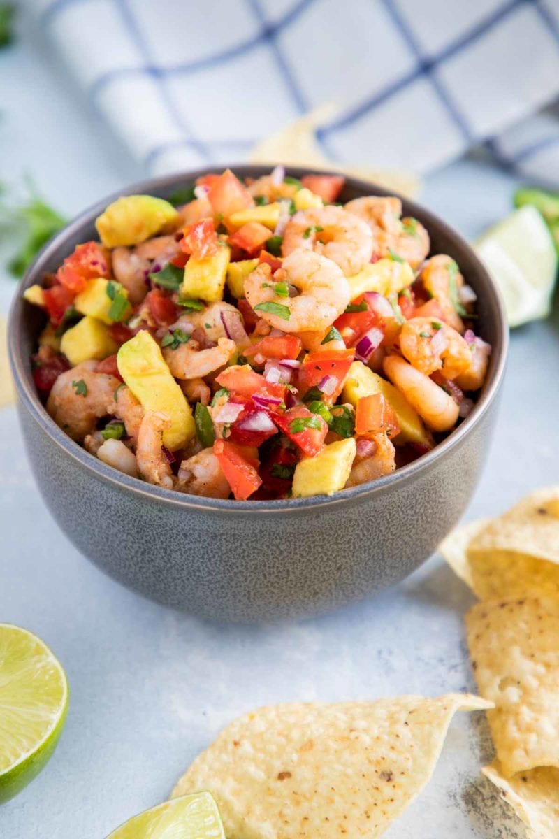 Avocado Shrimp Salsa in a grey bowl with corn chips and lime wedges on the side. 