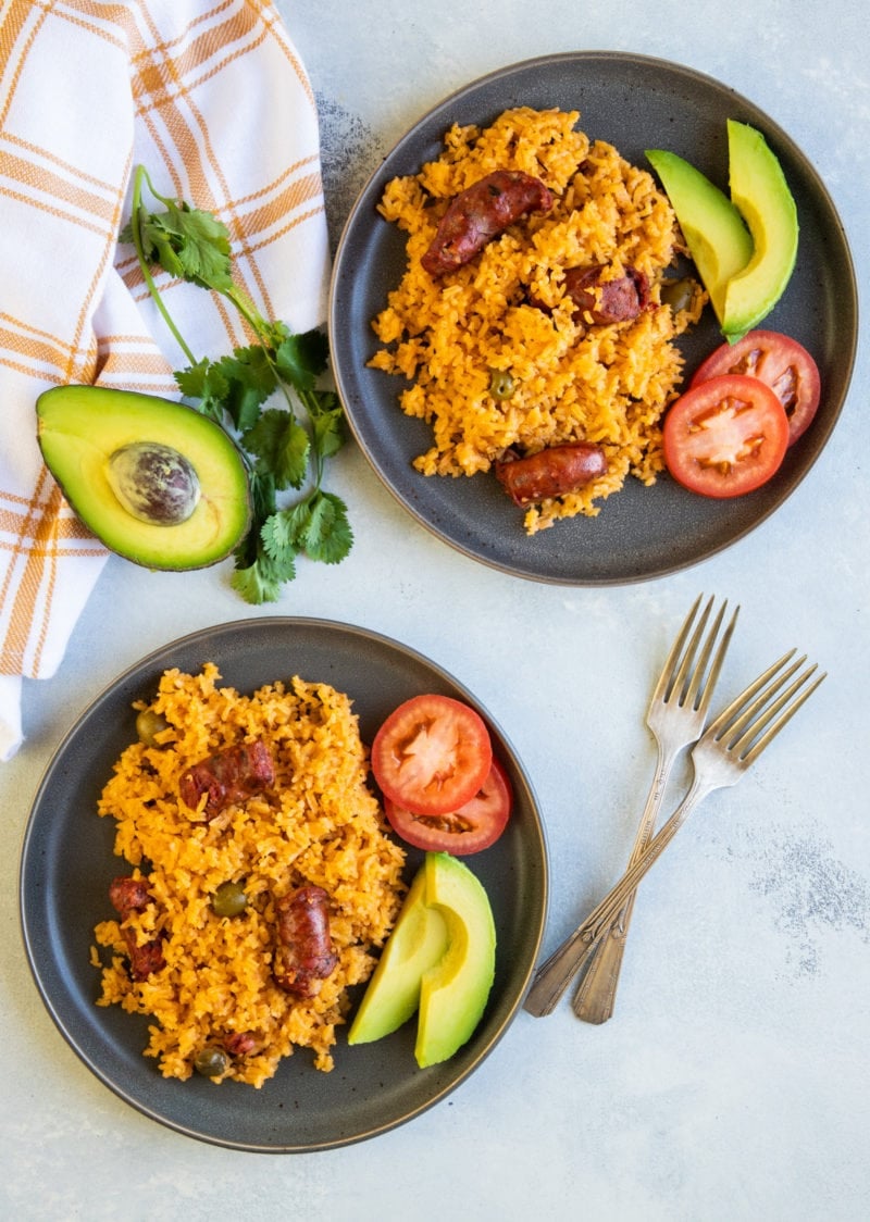 Locrio de Longaniza served on two plates with sliced avocado and tomato.