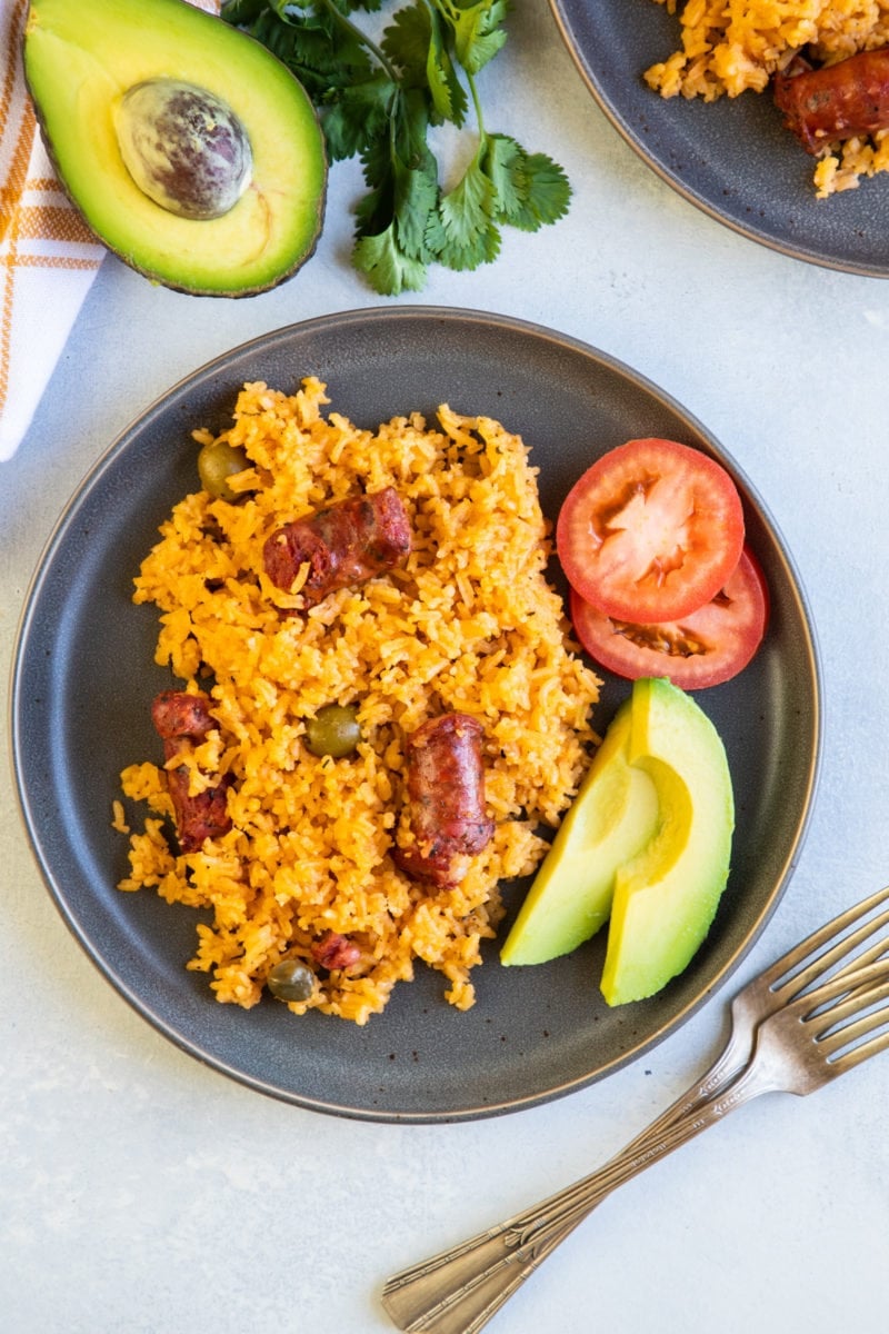 Over head shot of rice with sausage served on a plate with tomato and avocado on the side. 