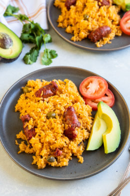 Locrio de Longaniza served on a plate with avocado and tomato.