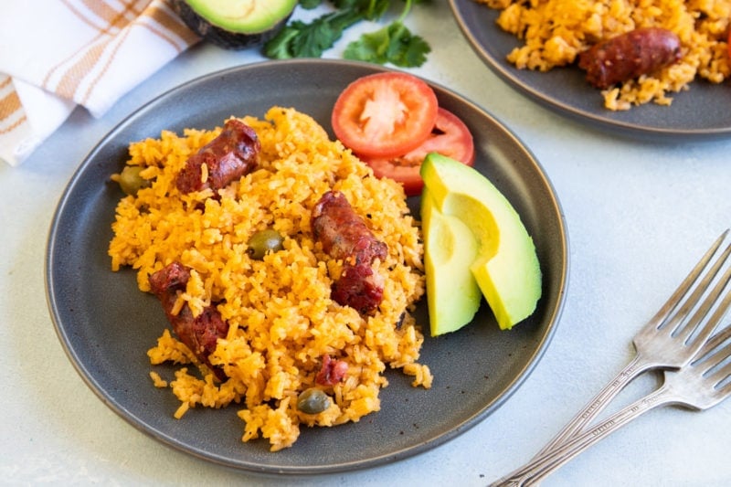 Rice with sausage served on a plate with tomato and avocado on the side. 