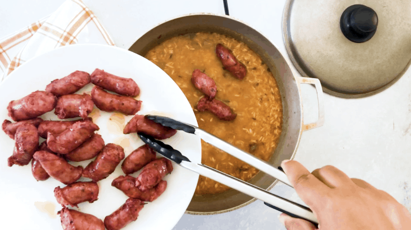 Sausages being placed back into the pan with the rice.