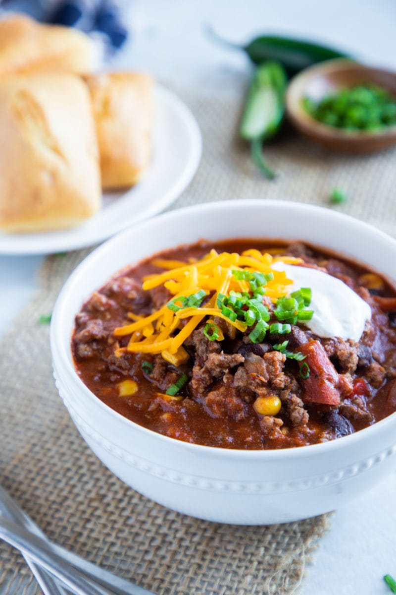 Chili servido en tazón blanco cubierto con queso, crema agria y cebolleta. 