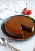 Chocolate flan served on a grey platter with strawberries on the side