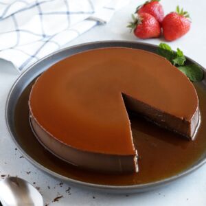 Chocolate flan served on a grey platter with strawberries on the side