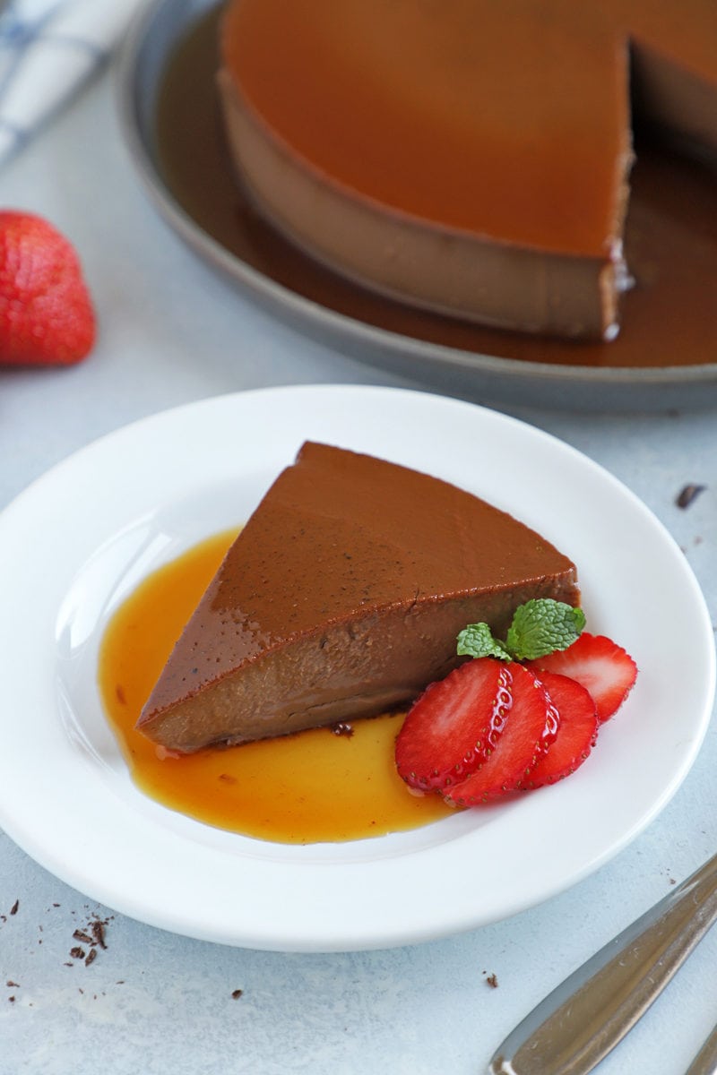 close up of chocolate flan slice served with strawberries on the side